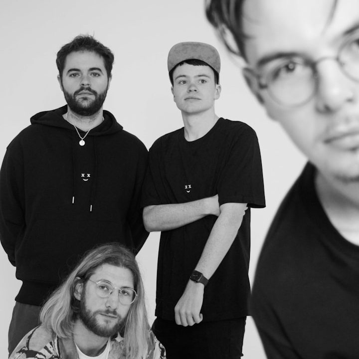 Four young men posing together, two standing in the back and two kneeling in front.