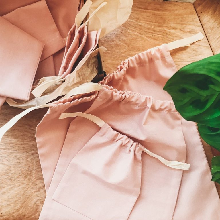 Brown and beige fabric bags on a wooden surface, surrounded by green leaves.