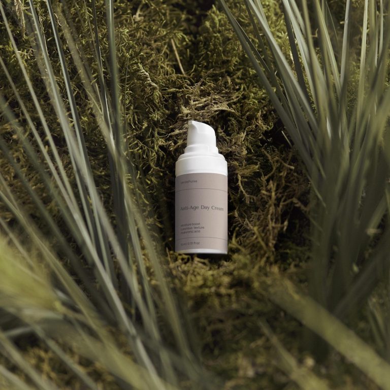Bottle of skincare product resting on moss surrounded by green plants.