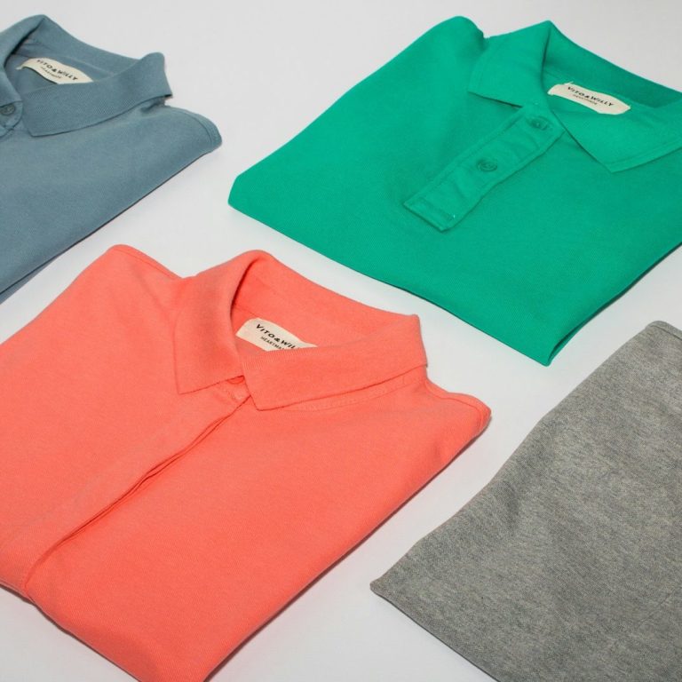 Four folded polo shirts in blue, green, coral, and gray arranged neatly.